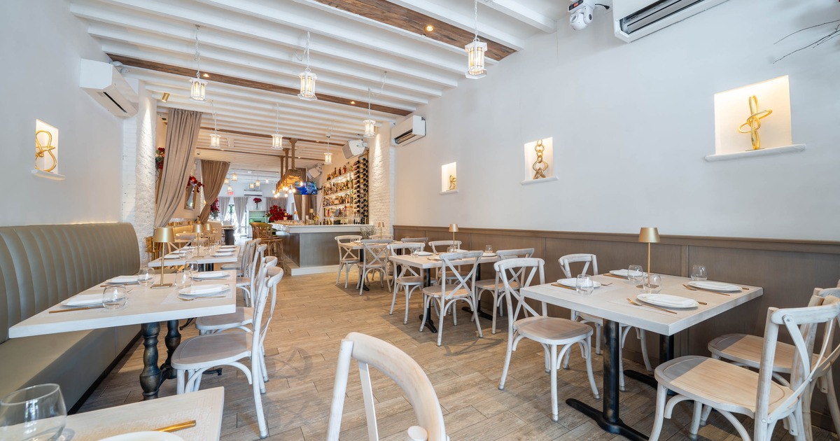 A modern restaurant interior with white walls, wooden beams, light wooden tables, and white chairs