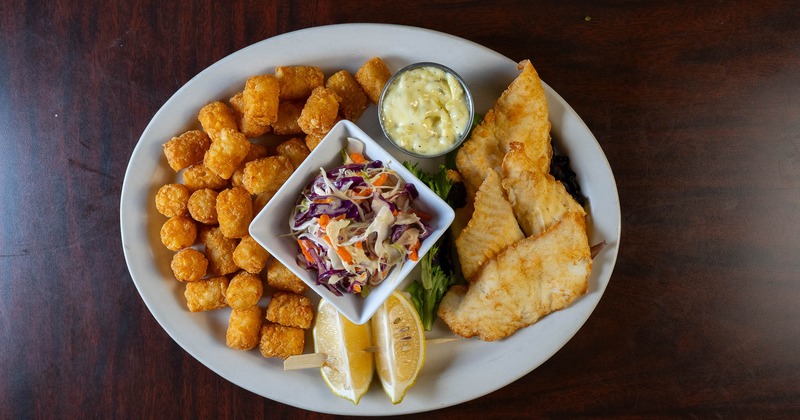Halibut fish and chips served with slaw, tartar sauce, lemon wedges, and fries