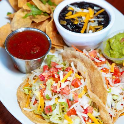 Tacos served with chips, black beans, guacamole and red sauce.