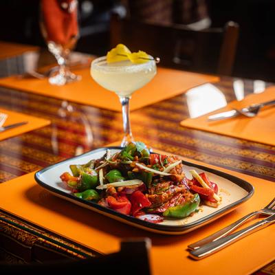 Chili curry chicken plate served on an ornate table with a yellow cocktail.