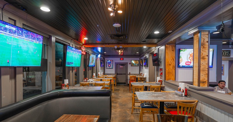 Interior of a sports bar with tables, booths, and multiple televisions displaying sports