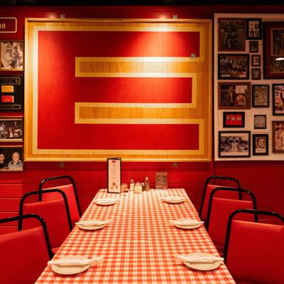A table with red checkered tablecloth, plates, and red chairs, set in front of a decorated red wall.