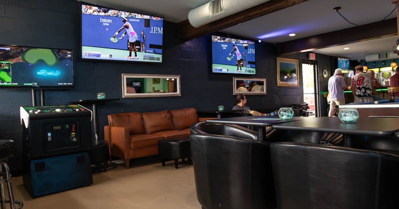 Interior space with seating, arcade golf game, and wall mounted TV screens