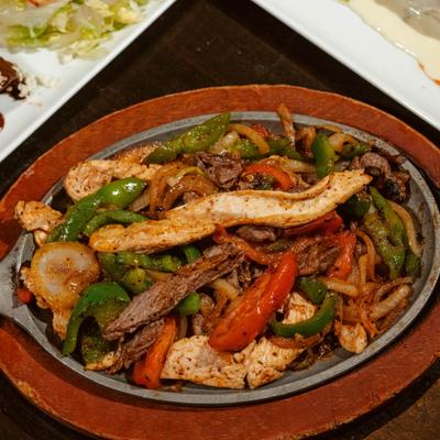 Chicken fajitas with peppers and onions, served in a skillet on a wooden base.