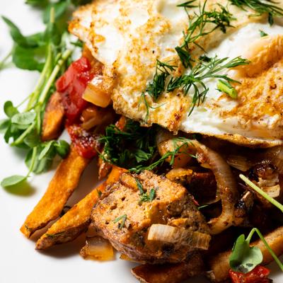 Breakfast hash topped with fried eggs and herbs, close-up.