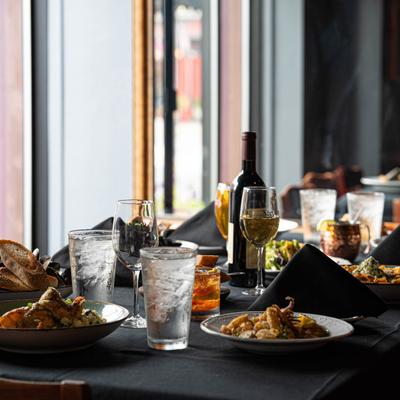 A dimly lit dining table with elegant black cloth is set with various dishes, wine, and drinks