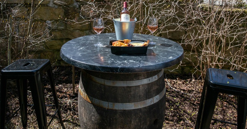 Exterior, a wooden barrel table with a dish and wine , and two bar stools