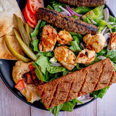 Mixed grill platter served over fresh salad with hummus and pita bread.