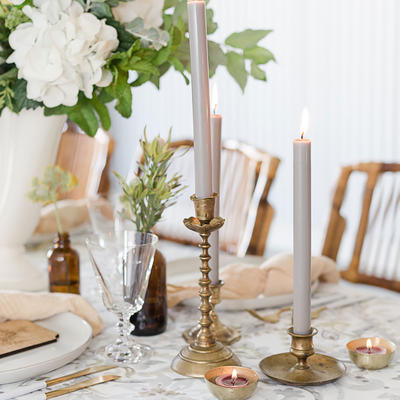 Elegant dining table with tall white candles , surrounded by delicate flowers and greenery