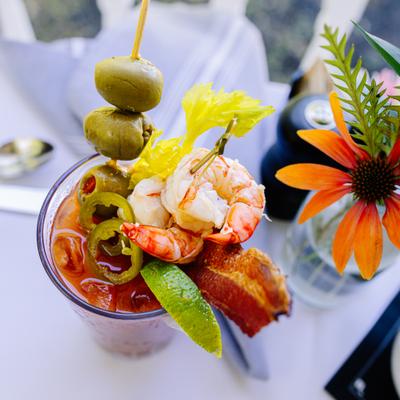 Bloody Mary cocktail garnished with shrimp, olives, bacon, and lime.