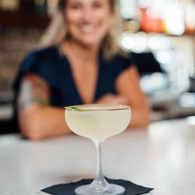 Cocktail in a coupe glass on a bar, bartender out of focus