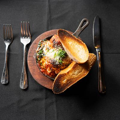 Beef meatballs and grilled bread set on a black tablecloth with two forks and a knife