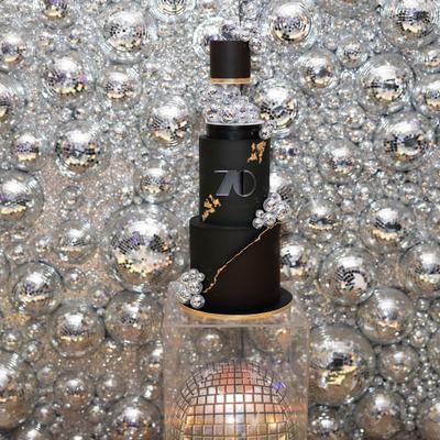Black tiered cake with a mirrored silver backdrop.