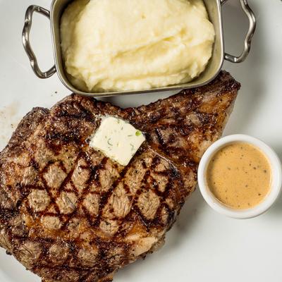 Grilled bone in steak with butter, gravy, and mashed potatoes.