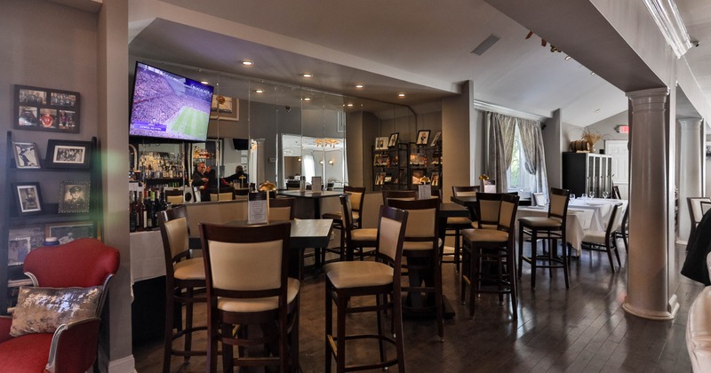 Interior of a modern restaurant with high tables and chairs, a wall-mounted TV, and a bar area