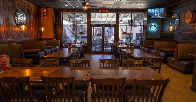 Interior with wooden tables, chairs, booth seating, pendant lights and large windows.