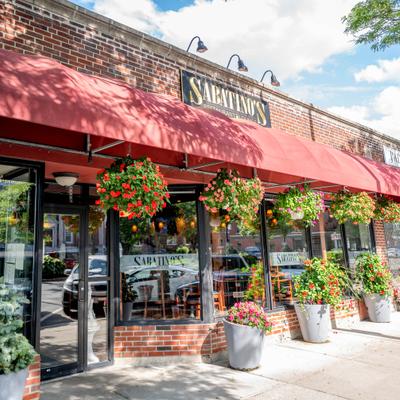 Storefront with signage, red awning, hanging plants and large windows.