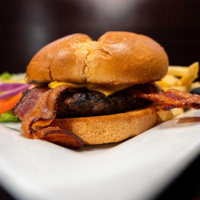 Close-up of a bacon cheeseburger with fries in the background.