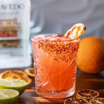 Pink pisco cocktail with chili rim, citrus garnish, and fresh lime halves.