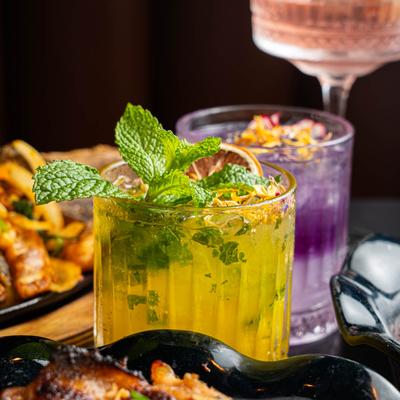 Colorful cocktails served with assorted food plates, close up.