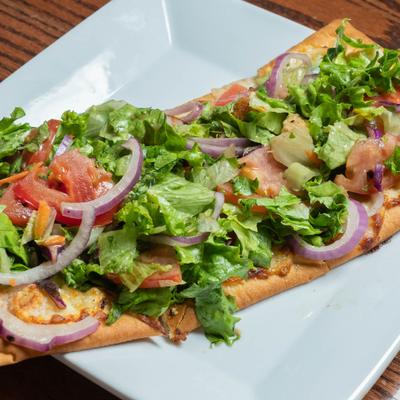 Flatbread pizza topped with fresh salad ingredients.