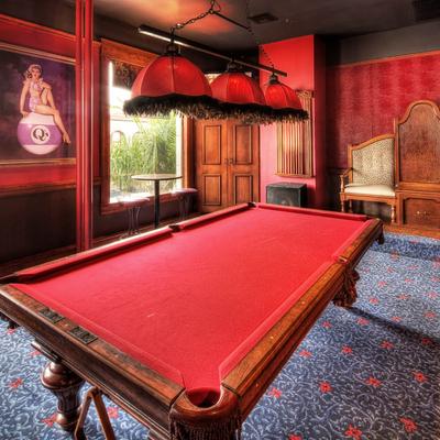 Luxurious room with red walls, featuring a red pool table under ornate hanging lights