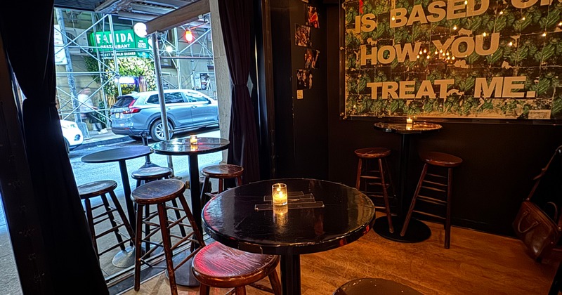A dimly lit bar area with wooden walls featuring a long bar counter with stools