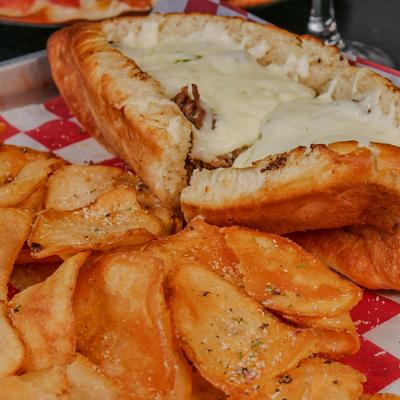 Philly cheesesteak sandwich served with potato chips.