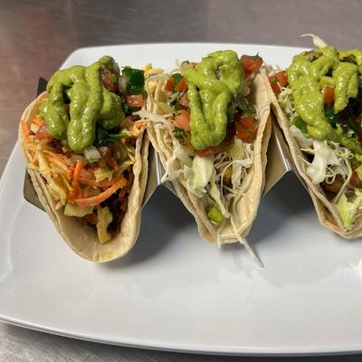 A trio of tacos topped with green avocado sauce.