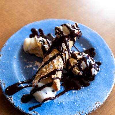 Cannoli dessert topped with chocolate drizzle on a blue plate.