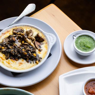 Oaxacan cheese dip topped with mushrooms and corn beside a cup of green sauce.