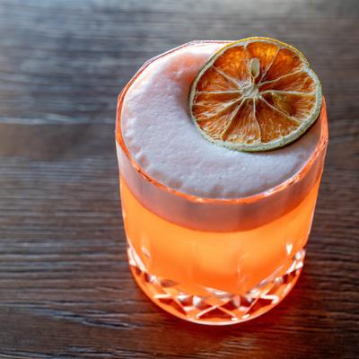A vibrant cocktail with a frothy top and a dried orange slice garnish.