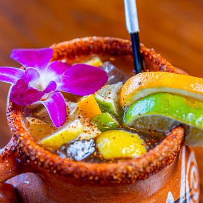 Cantarito drink served in a clay mug, garnished with lime and lemon wedges, and a pink orchid.