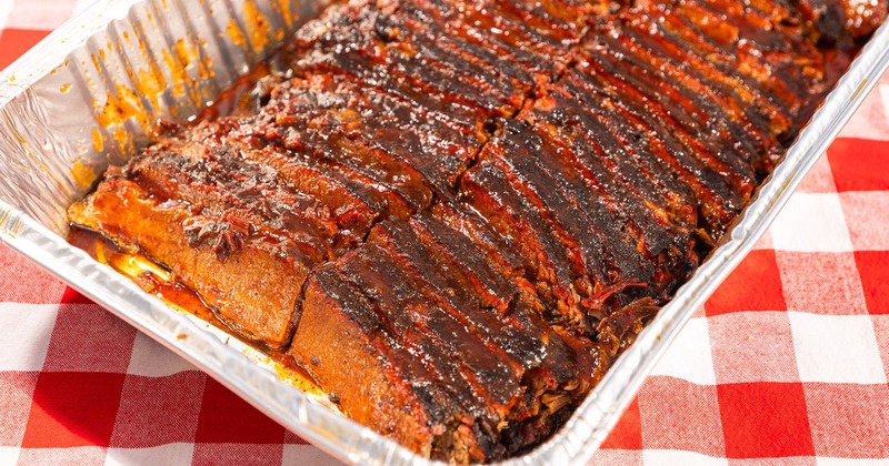 Barbequed brisket in a foil dish, presented on a red and white checkered tablecloth