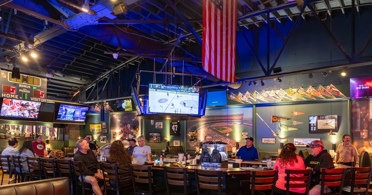 Bar area with a counter and patrons seated at bar watching at screens