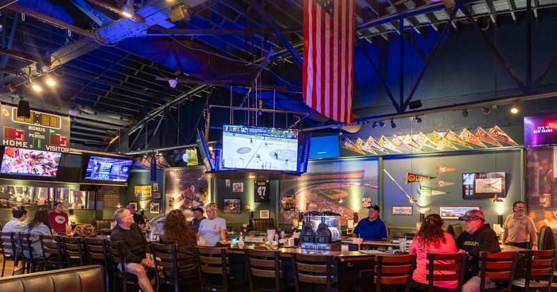 Bar area with a counter and patrons seated at bar watching at screens