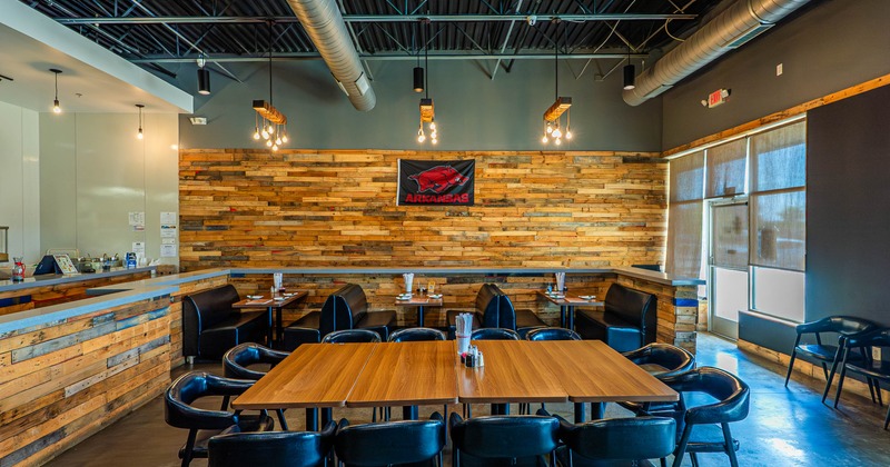 A restaurant interior with wooden walls and furniture, featuring black leather chairs and exposed ceiling fixtures