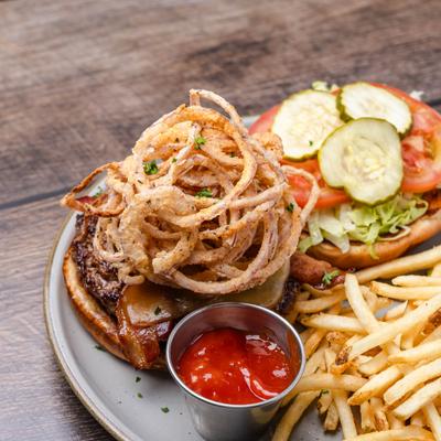 Bacon burger topped with crispy onions, served alongside fries and ketchup.