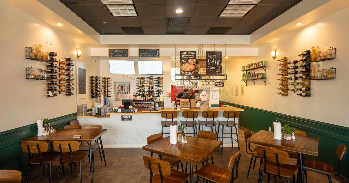 Interior - wooden tables & chairs; counter with high stools in the background.
