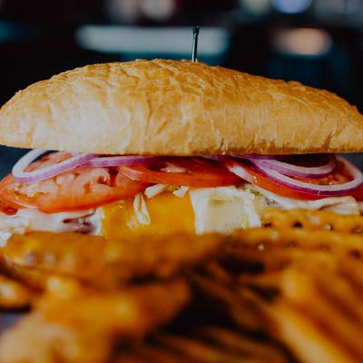 A close-up of a sandwich with cheese, tomato, onions, and waffle fries in the foreground.