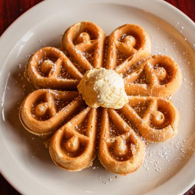 A flower-shaped Belgian waffle topped with a dollop of butter.
