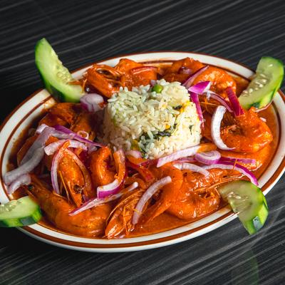Shrimp in a red sauce with rice, red onion slices, and cucumber garnish on a plate.