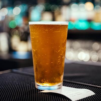 A glass of beer sitting on bar counter mat in the day time.