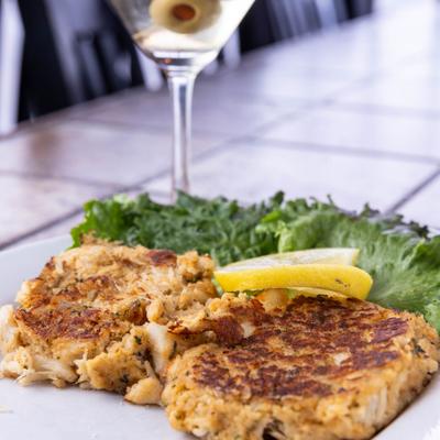 Crab cakes with lemon wedges on lettuce, accompanied with a martini.