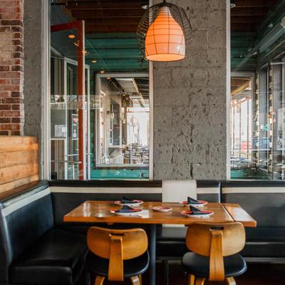 Set table with booth seating and chairs, pendant light, windows.