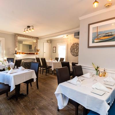 Dining room with white-clothed tables, dark chairs and wood flooring.