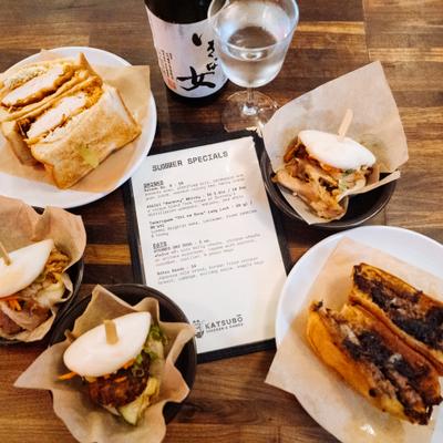 Assorted sandwiches and bao buns with a printed menu and drinks on a table.