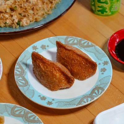 Fried tofu pouch pieces on blue and white patterned plate, accompanied with other dishes.