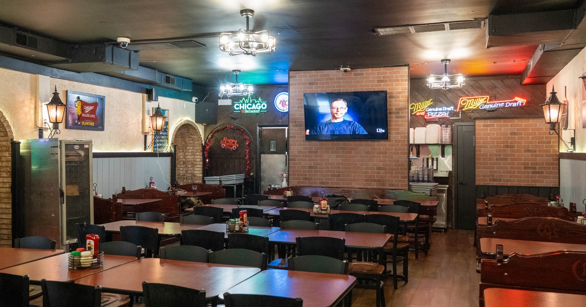 Interior of a casual restaurant with wooden tables and chairs, brick walls, a mounted TV