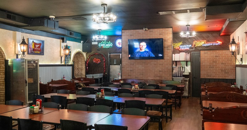 Interior of a casual restaurant with wooden tables and chairs, brick walls, a mounted TV